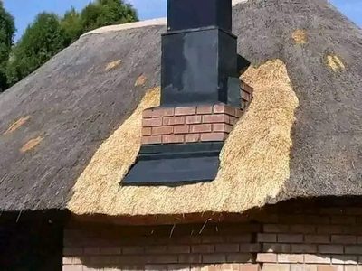 Close detail of a thatch roof neatly finished around a brick and steel chimney.