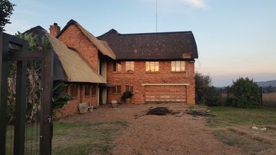 A double-storey face-brick home with a large thatch roof, photographed in early morning light.