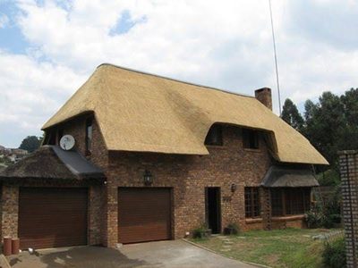 A large face-brick family home with a double garage and a sweeping thatch roof with a dormer window.