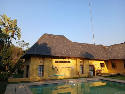 A home with warm yellow walls and a sweeping thatch roof, swimming pool in the foreground.