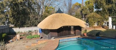 A low, rounded thatch-roofed lapa beside a swimming pool in a landscaped garden.